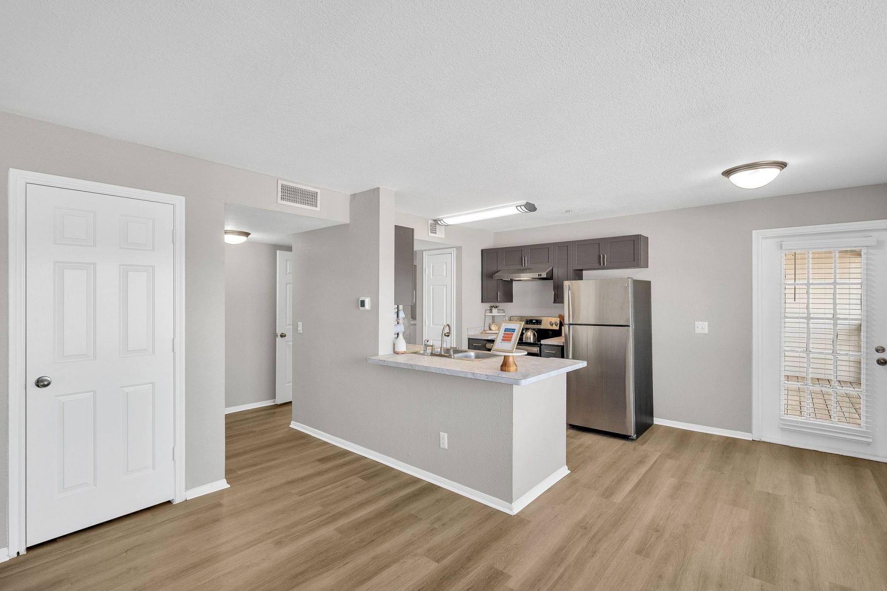 Empty room with wood floors, ceiling fan, and sliding glass door leading to a patio with vertical blinds at Apex West Midown.